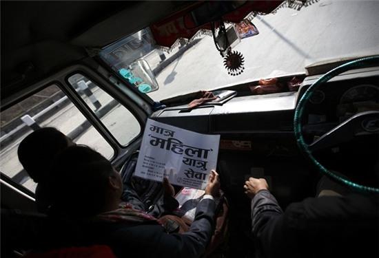 Một phụ nữ đọc dòng chữ trên tờ giấy được dán trước cửa kính xe buýt, dòng chữ bằng tiếng Nepal có nghĩa 