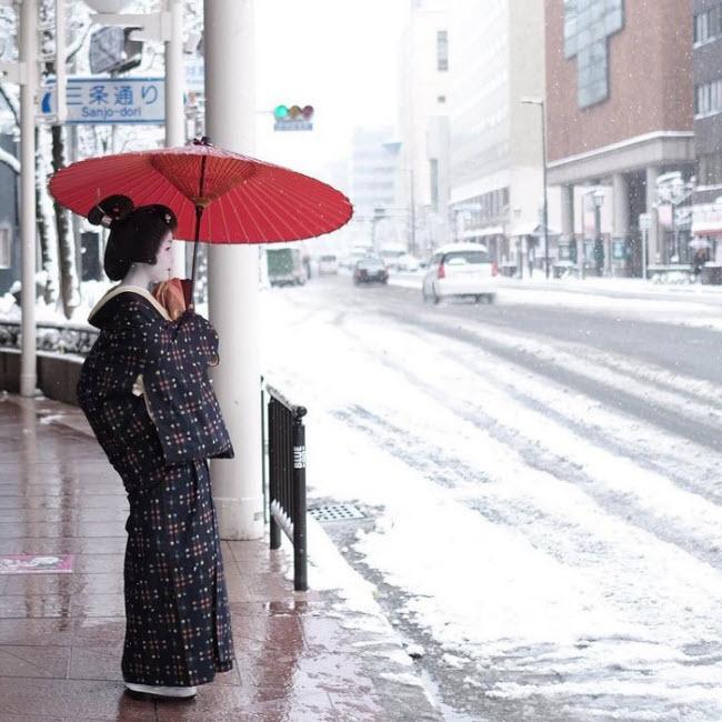 Một geisha cầm ô đứng ngắm tuyết rơi trên đường phố ở Kyoto.