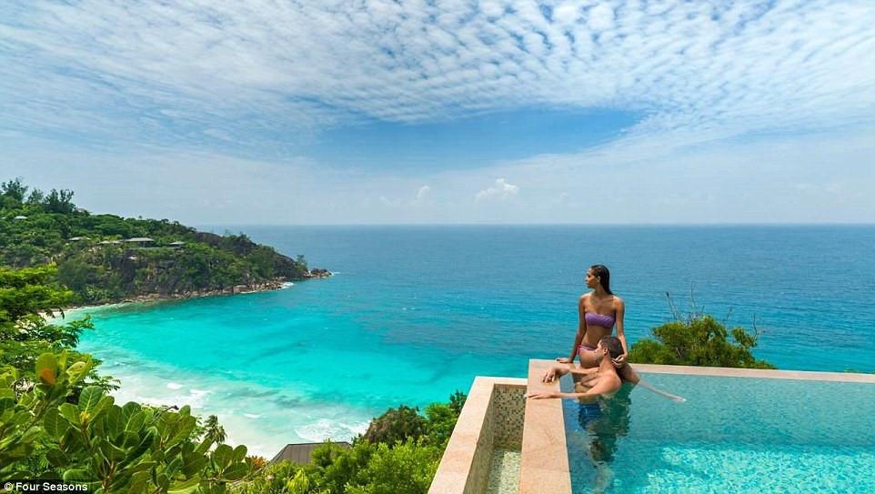 Khu nghỉ dưỡng Four Seasons, Seychelles: Một cặp đôi cùng chiêm ngưỡng khung cảnh ấn tượng với màu xanh của cây cối nổi bật trên màu biển từ bể bơi vô cực của Four Seasons.