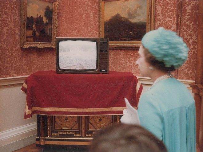 Bên trong cung điện, chiếc tivi đang phát sóng cảnh đám đông bên ngoài đang hân hoan chờ đón cô dâu chú rể ra mắt.