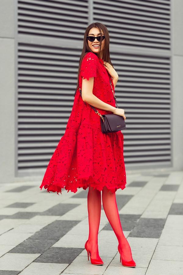 Lệ Hằng giấu đường cong trong dáng váy chữ A rộng truyền thống được thực hiện trên nền vải ren. Người đẹp mang đến màu sắc mới cho thiết kế khi phối cùng túi đeo chéo, giày cao kết hợp cùng tất da đồng điệu sắc đỏ.