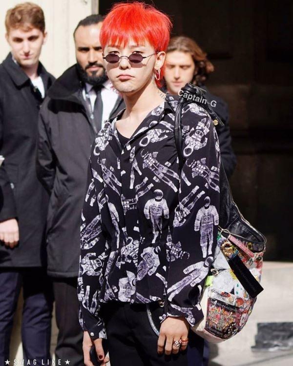 Năm 2017, G-Dragon trở thành tâm điểm chú ý khi xuất hiện tại Paris Fashion Week. Anh chàng nhuộm tóc đỏ nổi bật và diện outfit khá độc, lạ. Nam ca sĩ mặc áo sơ mi họa tiết rối mắt, khoác áo len bên ngoài. Điểm ấn tượng trên set đồ là chiếc túi đeo chéo to bản sặc sỡ, cùng đôi giày với những mảng màu thú vị. Ảnh: Swaglike