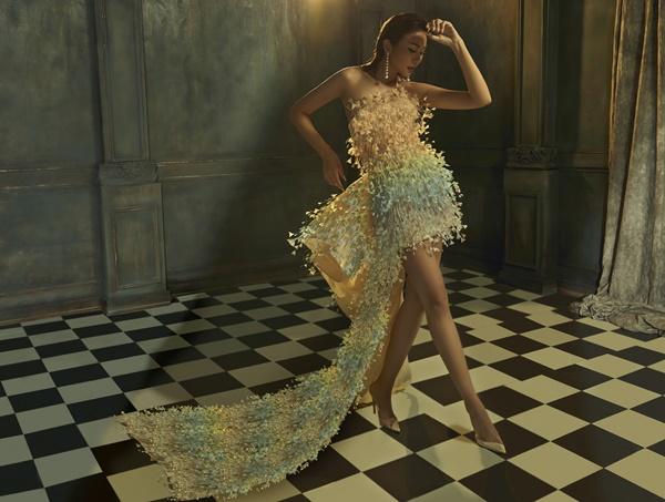 Thanh Hằng khoác lên mình chiếc đầm màu trắng được đính kết các cánh hoa theo dải màu cầu vồng, gợi liên tưởng đến các giọt sương sớm đang phản chiếu các sắc độ màu của tự nhiên.