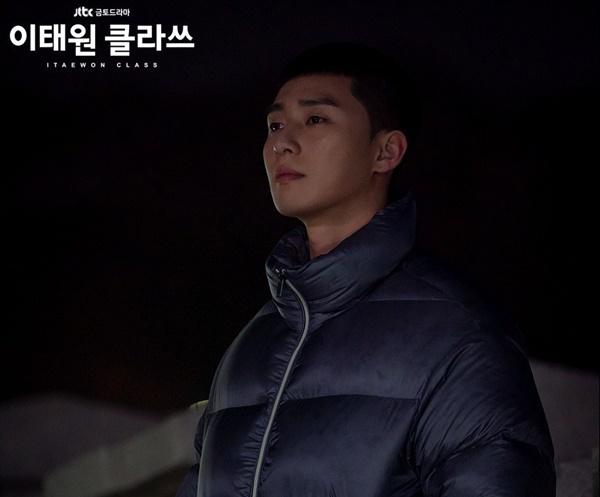 Bên cạnh những món đồ như áo thun trơn, hoodie tối màu hay quần thể thao, ông chủ quán nhậu Dan Bam cũng sở hữu nhiều loại áo big size để chống chọi với mùa đông ở Hàn Quốc. Ngoài kiểu tóc gọn gàng, áo jean wash big size bụi phủi cũng phần nào thể hiện cuộc đời đầy sóng gió của nhân vật họ Park. Áo phao phom ngắn và rộng giúp diễn viễn 32 tuổi tôn được bờ vai rộng, tăng thêm vẻ bụi bặm cho tổng thể. Để hợp với trang phục, anh thường phối cùng combat boots hay giày Air Force 1. Ảnh: JTBC.