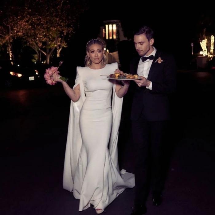 Hilary Duff là cũng là một nàng dâu thích ghi tên của hai vợ chồng lên váy cưới. Chiếc váy do Jenny Packham thiết kế trông khá hiện đại nhờ phần vai bồng bềnh hình yên ngựa và ống tay dài chạm sàn.