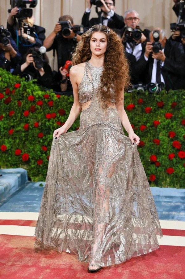 Với chủ đề Met Gala năm nay mang tên “In America: An Anthology of Fashion”, xoay quanh cốt lõi của phong cách Mỹ và tưởng nhớ những nhà thiết kế tài năng, các ngôi sao bước trên thảm đỏ trong trang phục lấp lánh, thể hiện vẻ cổ điển. Nằm trong top những sao nữ mặc đẹp nhất bữa tiệc thời trang do ELLE bình chọn là người mẫu Kaia Gerber. Con gái của Cindy Crawford khoe dáng trong chiếc váy của Alexander McQueen. Cô kết hợp cùng lối trang điểm và mái tóc gợi nhớ đến thời xưa.